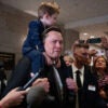 Elon Musk carries a young son piggyback-style.