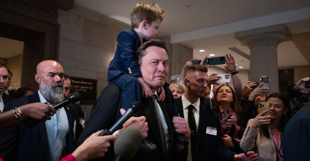 Elon Musk carries a young son piggyback-style.