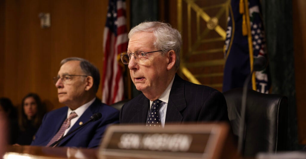 Mitch McConnell sits wearing a black suit and dark necktie.