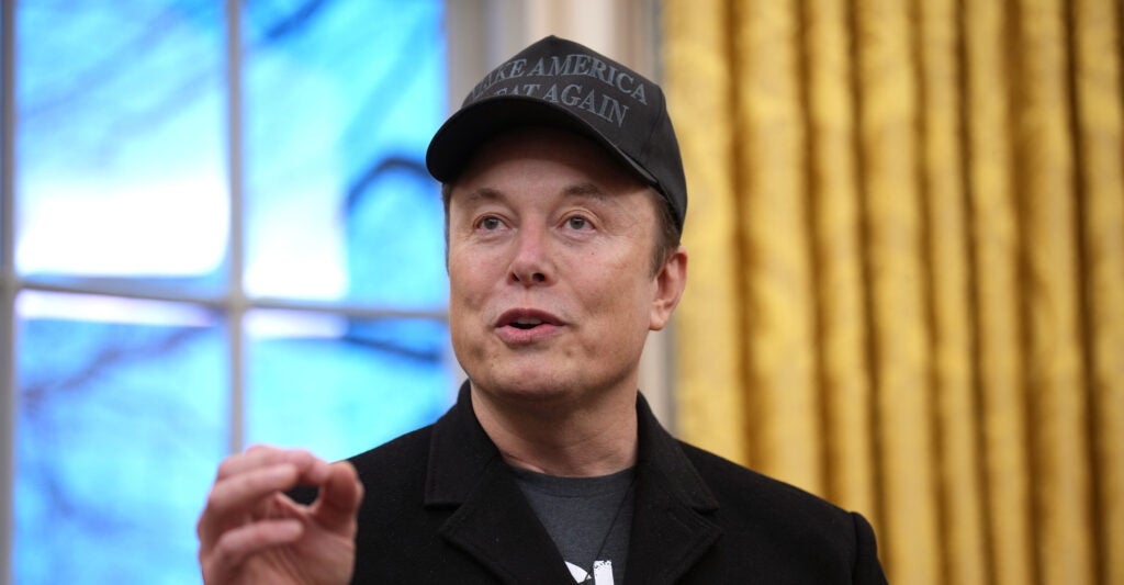Elon Musk wears a black MAGA hat.