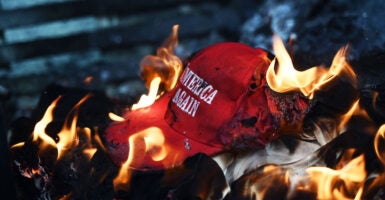 A "Make America Great Again" hat burns on top of a fire.