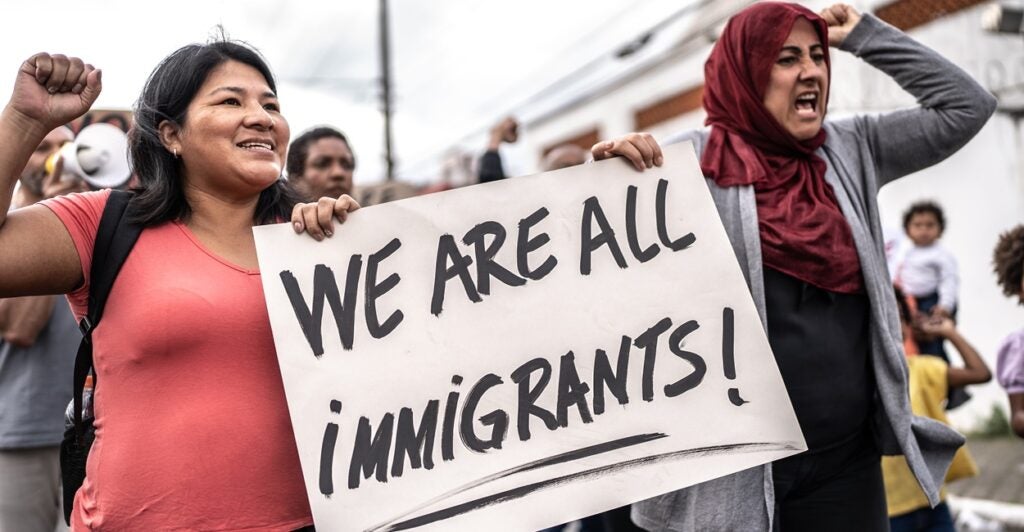 Two women shout as they hold signs protesting.
