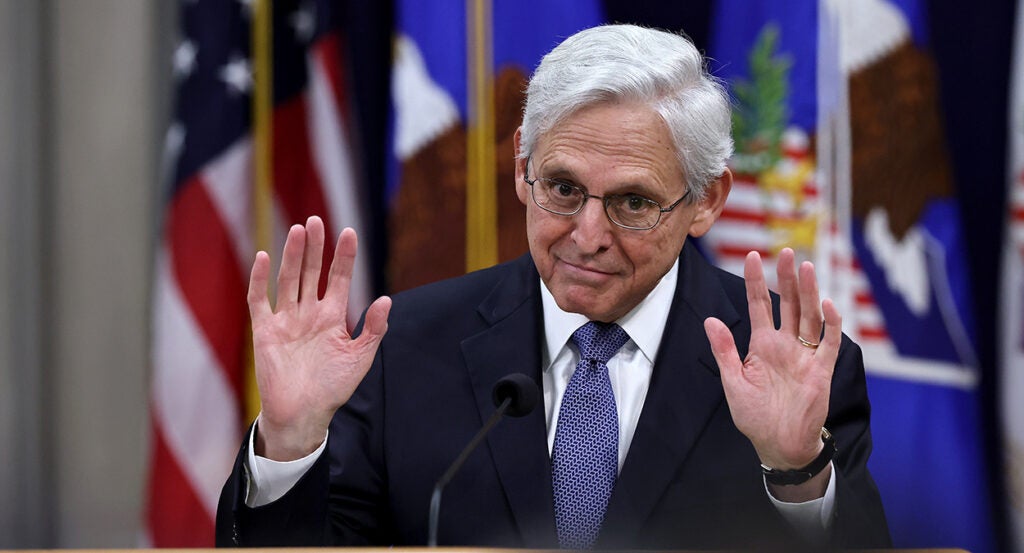 Merrick Garland in a suit raises his hands up
