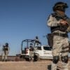 A member of the National Guard stands near the Mexico border holding a gun while dressed in military gear.