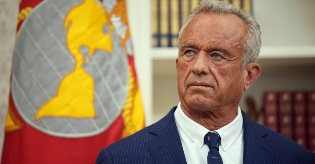 Robert F. Kennedy stands and listens to Donald Trump with his head turned slightly to his right.