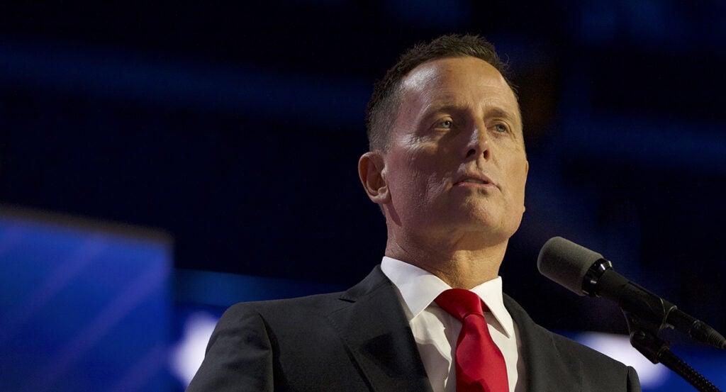 Ric Grenell speaks in a grey suit with a red tie