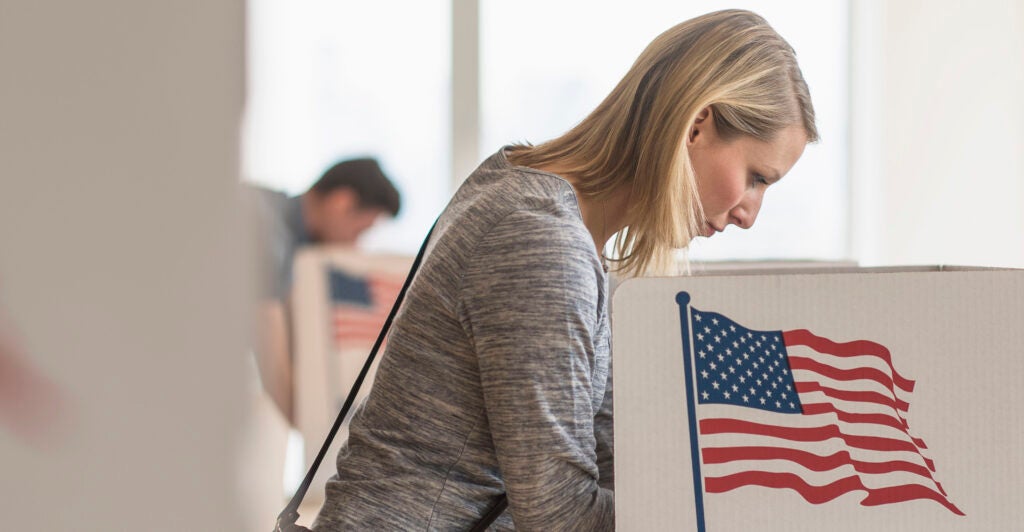 a blonde woman in a white outfit voting at a voting station with an American flag on the side of it