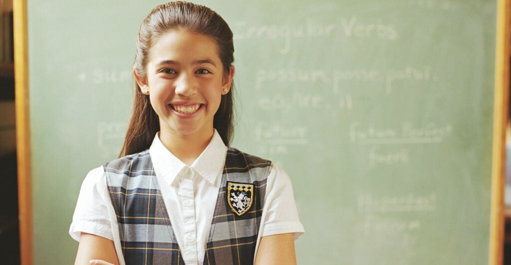 A school girl in a uniform poses for a photo while standing.