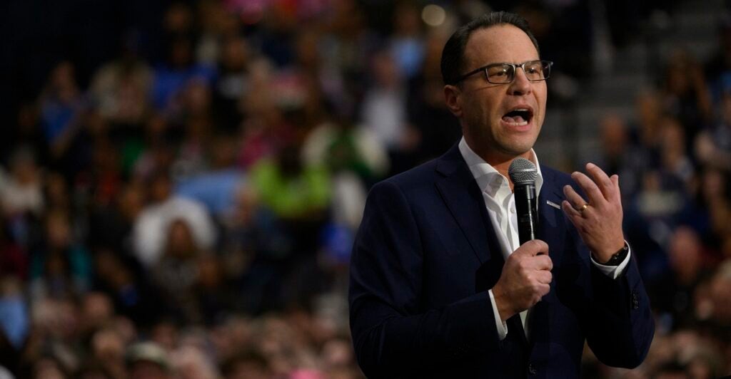 Josh Shapiro stands while holding a microphone as he talks during a rally.