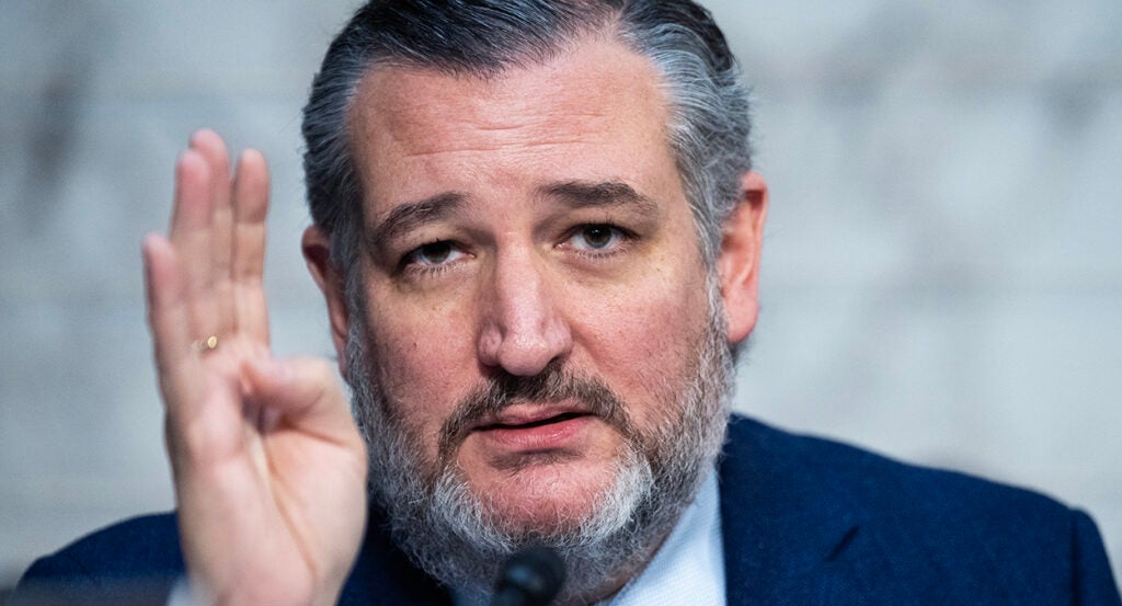 Ted Cruz in a suit holds up his hand