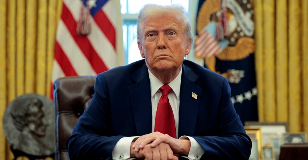 Donald Trump sits at his desk in the White House with his hands folded in front of him.