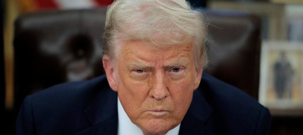 Donald Trump sits at his desk in the White House and glares ahead.