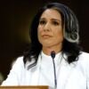 Tulsi Gabbard sits with a microphone in front of her and looks ahead.