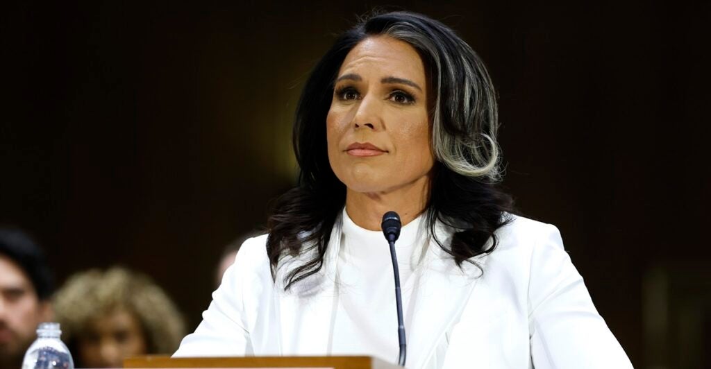 Tulsi Gabbard sits with a microphone in front of her and looks ahead.