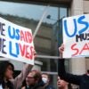 A man and a woman hold up signs saying that USAID must be saved while standing in front of a building.