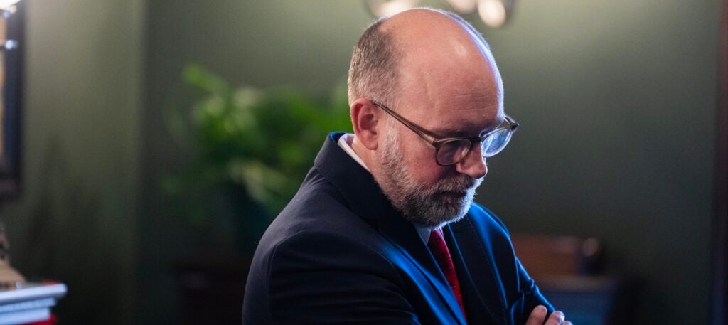 Russell Vought stands in a room with his arms folded.
