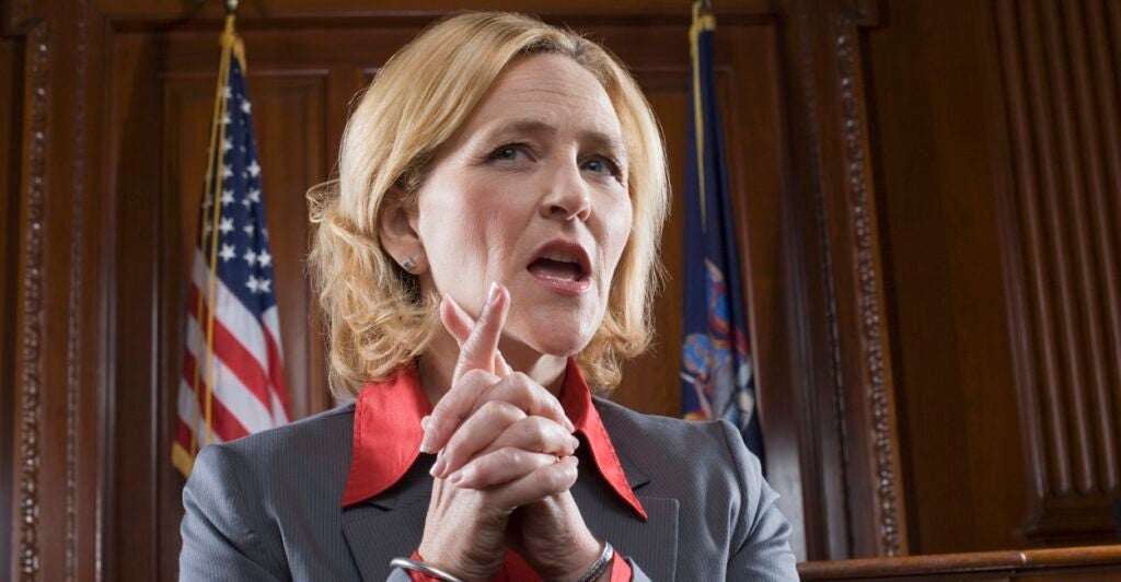 A female lawyer clasps her hand together as she talks in court.