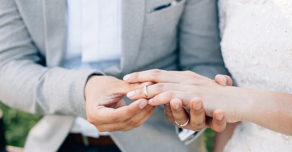 A groom puts the ring on the bride's finger.