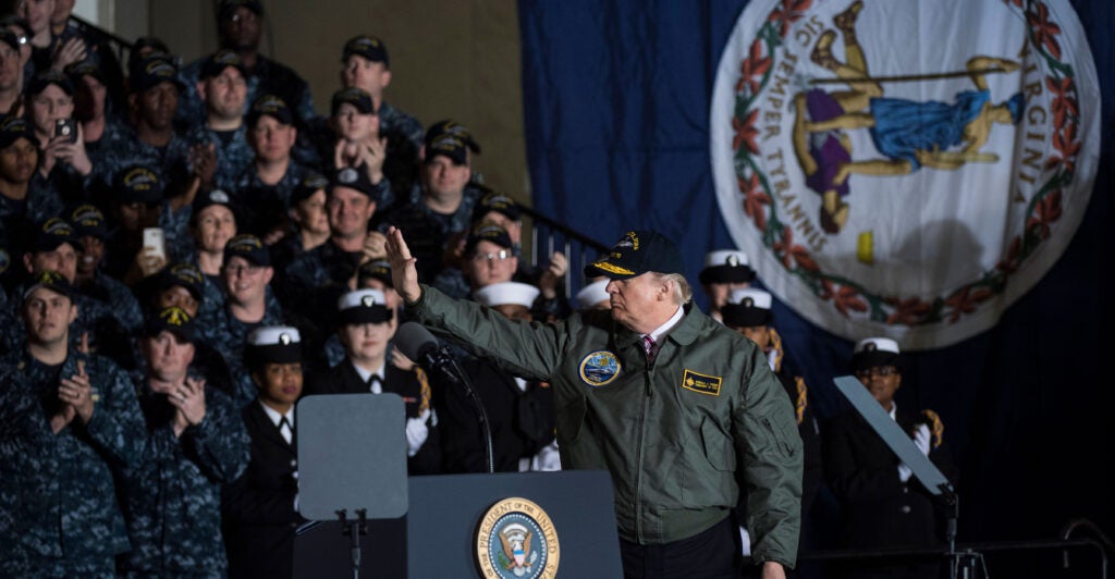 President Donald Trump waves after speaking to Navy and shipyard personnel aboard the nuclear aircraft carrier Gerald R. Ford at Newport News Shipbuilding in Newport News, Va., eight years ago this month on March 2, 2017. A large Virginia state flag hangs vertically on the wall at right.