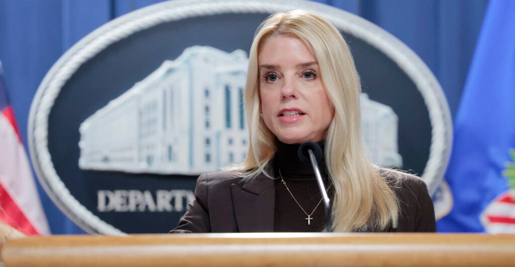 Attorney General Pam Bondi speaks in front of the Department of Justice symbol.