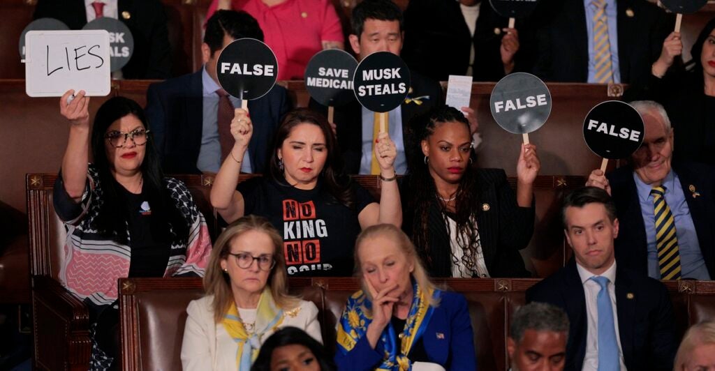 Democrats sit in seats and hold up signs protesting Donald Trump's speech.