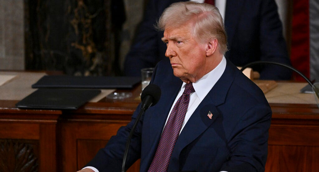 Donald Trump in a blue suit with an American flag pin looks skeptical