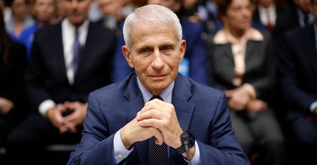 Anthony Fauci wears a blue suit as he sits with his hands clasped.