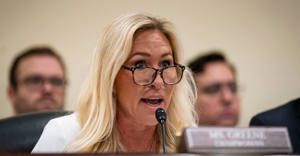 Marjorie Taylor Greene wears a white suit and black-rimmed glasses.