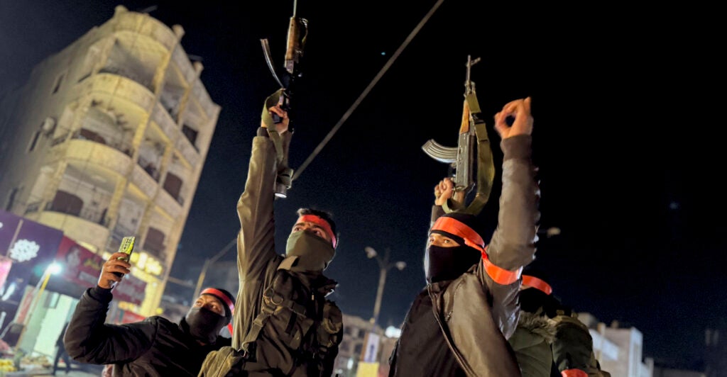 Masked armed forces of the new Syrian government raise their Kalashnikov rifles as they are being deployed to the coastal city of Latakia.