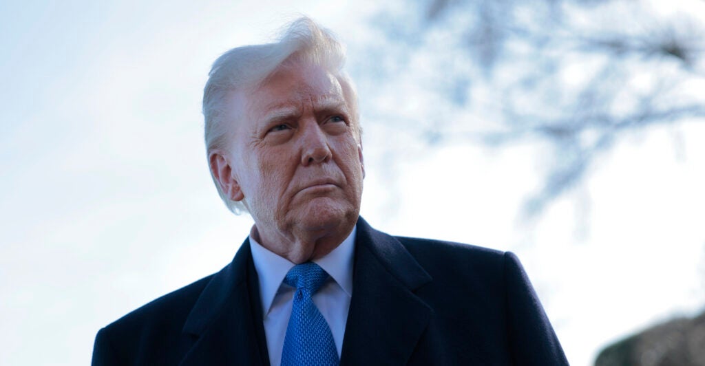 Donald Trump is outside wearing a black coat and light-blue necktie.