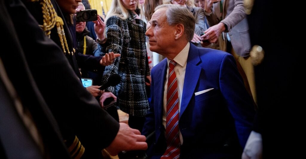 Greg Abbott is surrounded by a crowd as he looks up at a person.