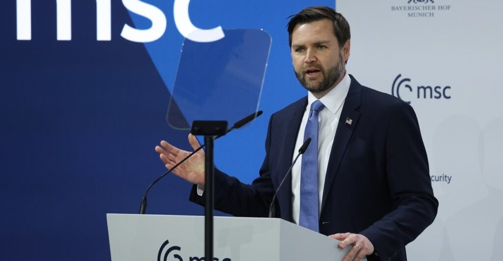 JD Vance stands at a podium with a microphone in front of him and talks while he raises his right hand.
