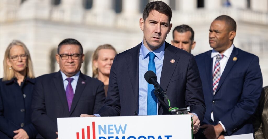 Josh Harder stands at a podium with a microphone and speaks and an outdoors press conference.