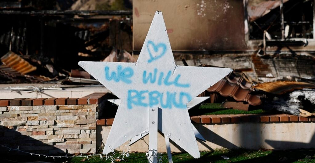 A handwritten sign posted in front of the ruins of the fires in Pasadena states they will rebuild.