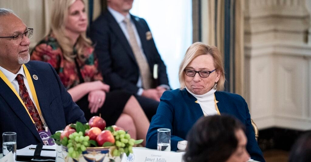 Maine Gov. Janet Mills sits at a table with an uncomfortable look on her face as President Donald Trump criticizes her policies.
