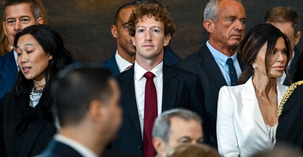 Mark Zuckerberg stands among some of the most power and rich people in the world staring ahead with no expression.