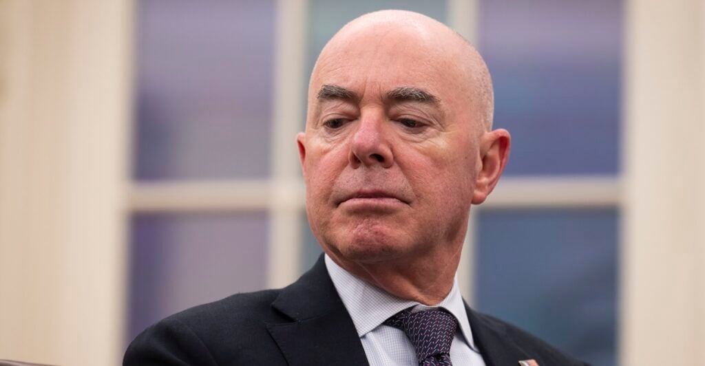 Alejandro Mayorkas listens and turns his head to his left while sitting down during a briefing.