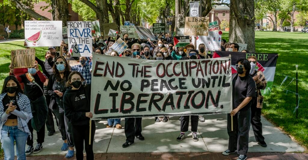Protesters walk down a sidewalk holding anti-Israel signs.