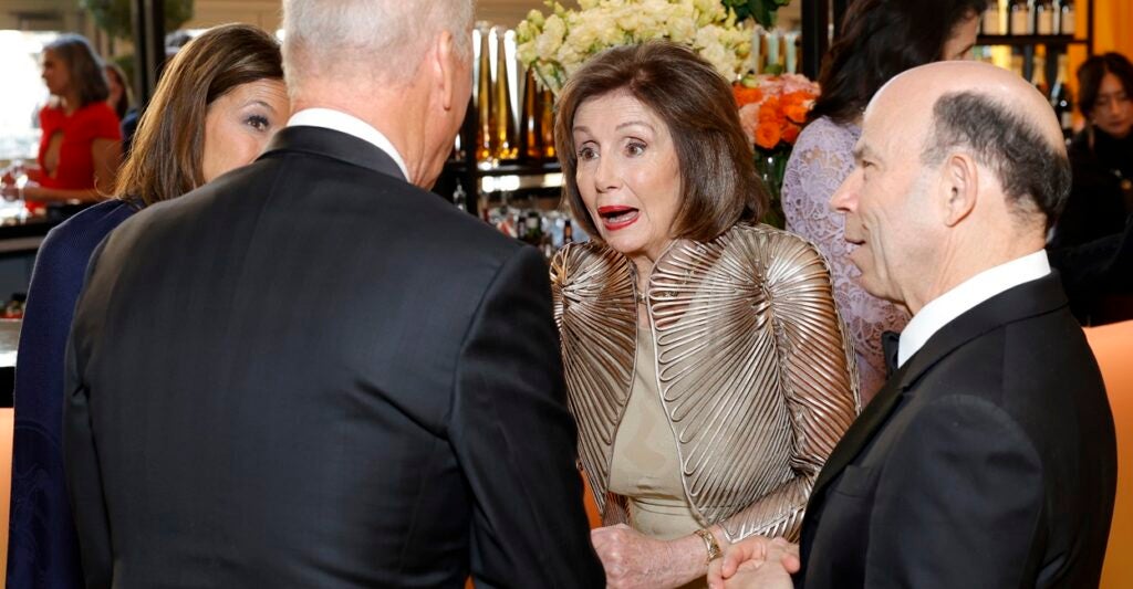 Nancy Pelosi talks with guests who are formed in a circle around her at a party.