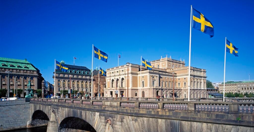 Swedish flags fly on a sunny day on a bridge in Sweden.