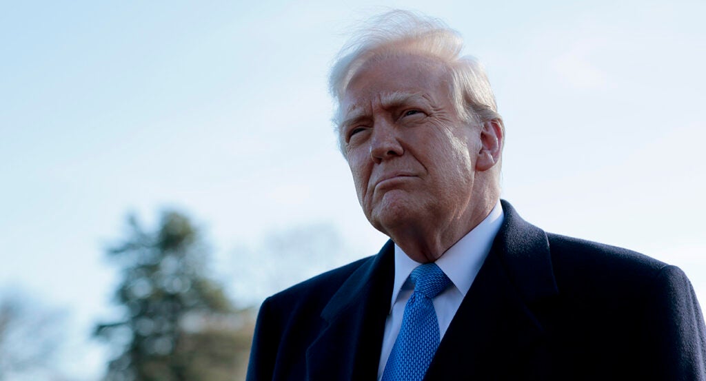 Donald Trump in a black suit with a blue tie looks bemused outside