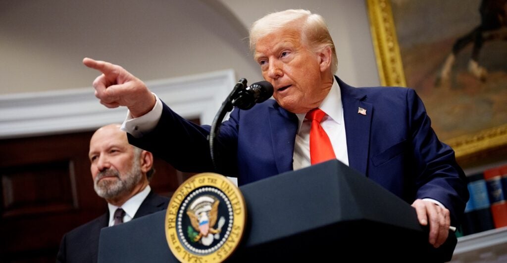 Donald Trump stands at a podium and points to a reporter who wants to ask a question at a press conference.