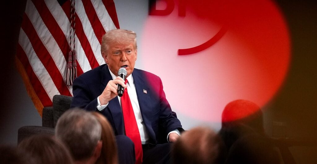 Donald Trump sits and holds a microphone in his right hand as he talks.