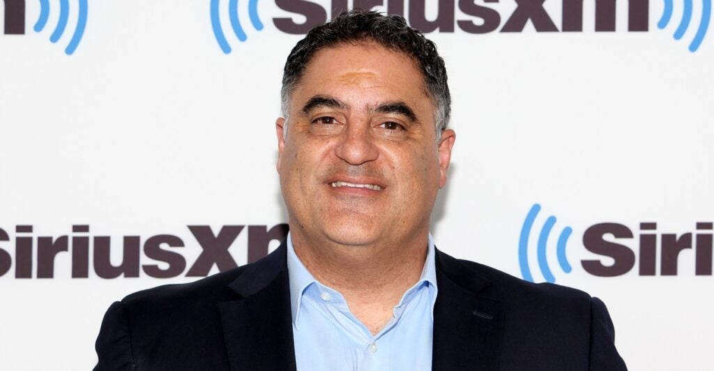 Cenk Uygur stands on a red carpet during an event and smiles at the camera.