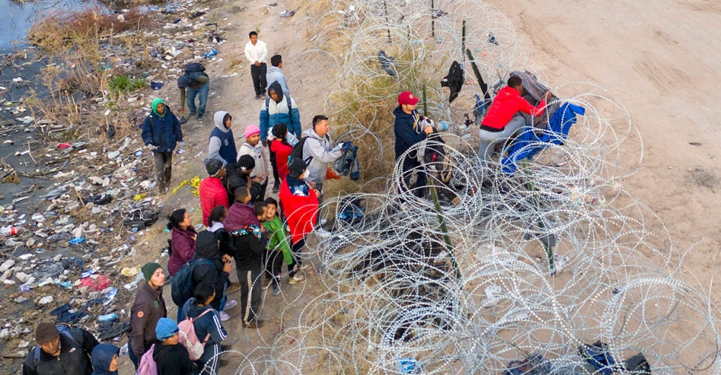 Illegal aliens try to pass over razor wire after crossing the border into El Paso, Texas.