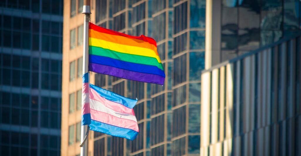 The transgender flag flies underneath the gay pride flag.
