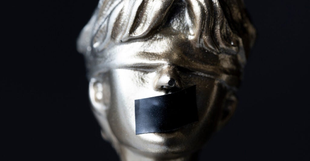 An image depicts Lady Justice with black tape over her mouth.