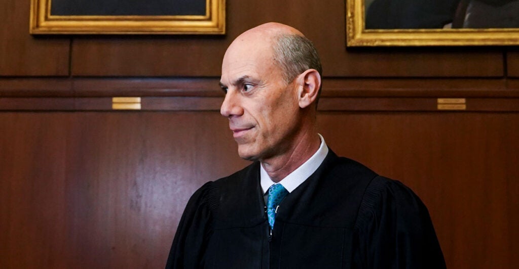 Judge James E. Boasberg stands in a black robe and blue tie in front of a wood panel wall