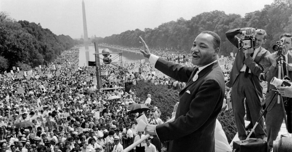in a black-and-white photo, Martin Luther King Jr. stares across a crowded Washington Mall before a speech with photographers taking pictures of him in the background
