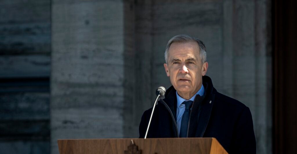 Mark Carney stands at a podium and looks out ahead with a microphone in front of him.
